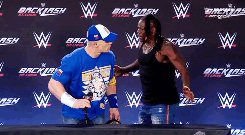 A Man Wearing A Blue Shirt That Says " Let 'S Go " Stands Next To Another Man GIF