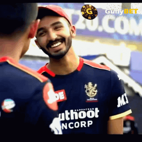 A Man Wearing A Blue Shirt That Says Uthoot Ncorp Is Smiling While Talking To Another Man . GIF