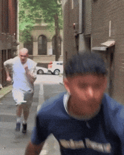 A Man Wearing A Blue Shirt That Says ' Washington ' On It Is Running Down A Street GIF