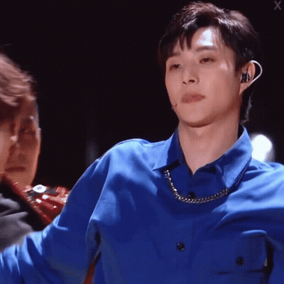 A Man Wearing A Blue Shirt With A Chain Around His Neck Looks At The Camera GIF