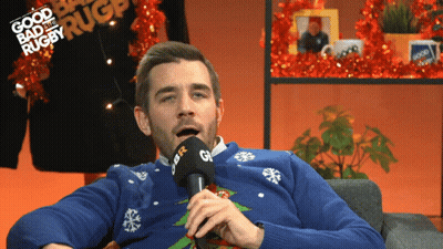 A Man Wearing A Blue Sweater Is Talking Into A Microphone With The Words Good Bad And Rugby Written In The Background GIF