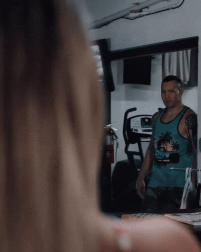 A Man Wearing A Blue Tank Top With Palm Trees On It Looks At Himself In A Mirror GIF