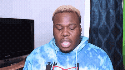 A Man Wearing A Blue Tie Dye Hoodie And Glasses Is Standing In Front Of A Television . GIF