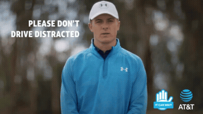 A Man Wearing A Blue Under Armour Jacket Stands In Front Of A Sign That Says Please Do N't Drive Distracted GIF