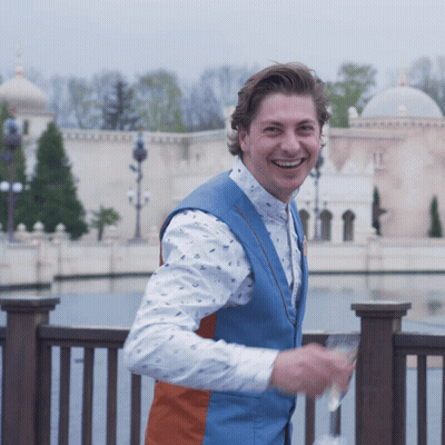 A Man Wearing A Blue Vest And A White Shirt Smiles GIF