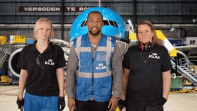 A Man Wearing A Blue Vest That Says Klm Stands Between Two Women GIF