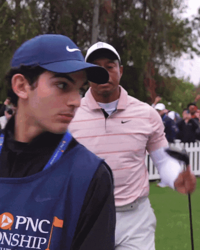 A Man Wearing A Blue Vest That Says Pnc On It Stands Next To A Man Holding A Golf Club GIF