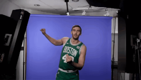 A Man Wearing A Boston Jersey Is Dancing In Front Of A Blue Backdrop GIF
