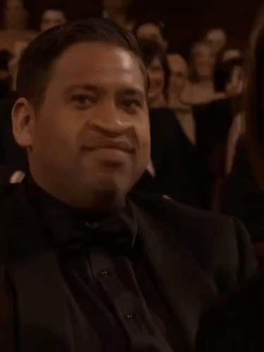 A Man Wearing A Bow Tie And A Ring Is Sitting In A Theatre . GIF