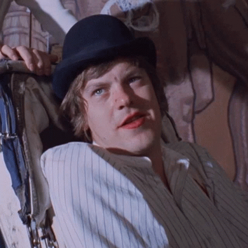 A Man Wearing A Bowler Hat And Striped Shirt Is Laying Down GIF