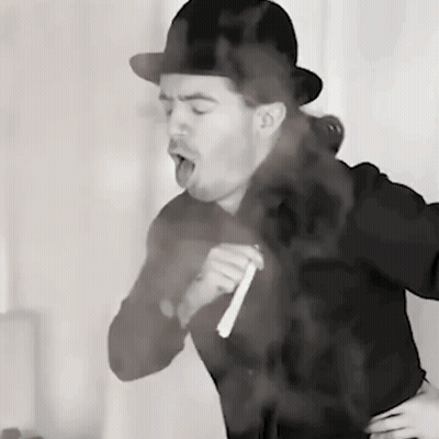 A Man Wearing A Bowler Hat Is Smoking A Cigarette In A Black And White Photo GIF