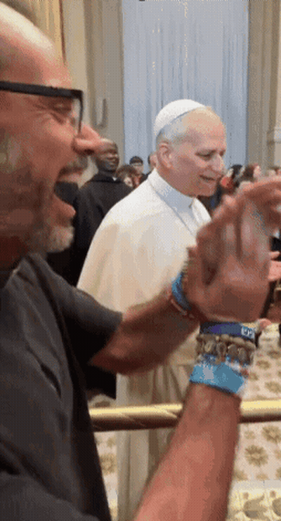A Man Wearing A Bracelet That Says ' Dc ' On It Stands Next To A Man Wearing A White Hat GIF