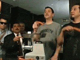 A Man Wearing A Brooklyn T-Shirt Stands In Front Of A Meat Grinder GIF