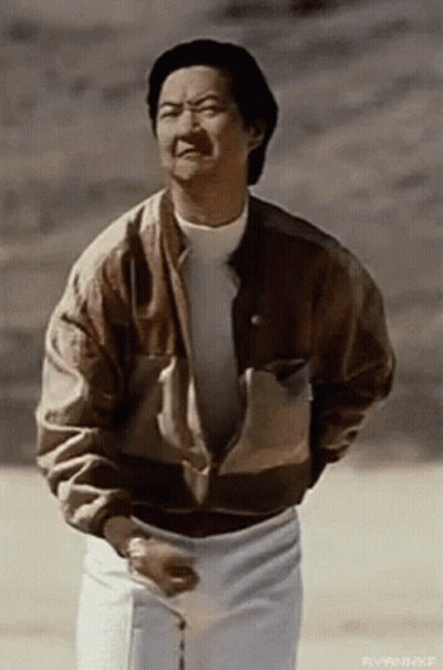 A Man Wearing A Brown Jacket And White Pants Is Standing In The Desert . GIF