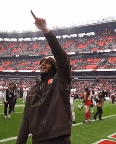 A Man Wearing A Brown Jacket With The Number 22 On It Stands On A Football Field GIF