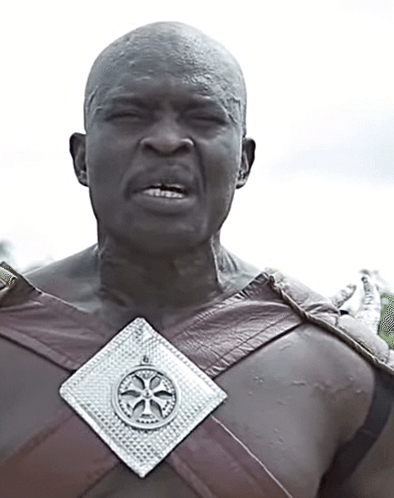 A Man Wearing A Brown Leather Vest With A Silver Medallion Around His Chest GIF