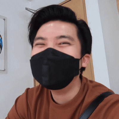 A Man Wearing A Brown Shirt And A Black Face Mask Smiles GIF