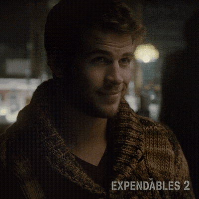 A Man Wearing A Brown Sweater With The Expendables 2 On The Bottom GIF