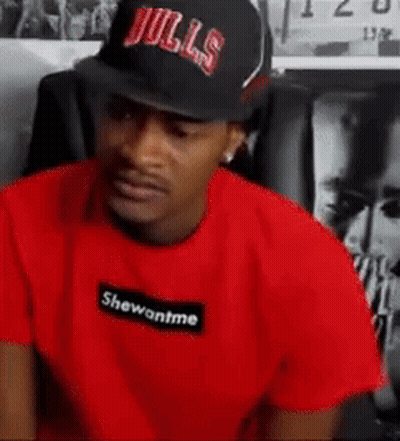 A Man Wearing A Bulls Hat And A Red T-Shirt Is Sitting In A Chair . GIF
