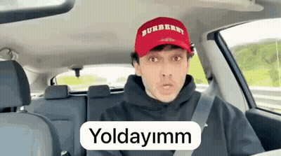 A Man Wearing A Burberry Hat Is Driving A Car And Talking . GIF
