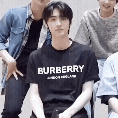 A Man Wearing A Burberry London England T-Shirt Is Sitting In Front Of A Group Of Men . GIF