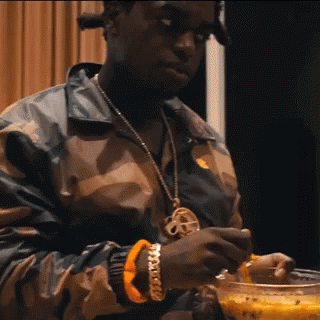 A Man Wearing A Camouflage Jacket Is Holding A Bowl Of Food . GIF