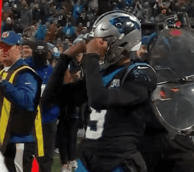A Man Wearing A Carolina Panthers Helmet Stands In Front Of A Crowd . GIF