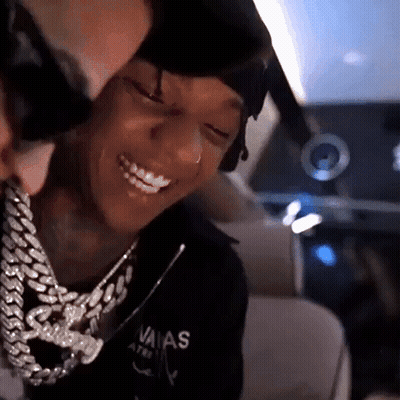 A Man Wearing A Chain Around His Neck Is Smiling While Another Man Looks On . GIF
