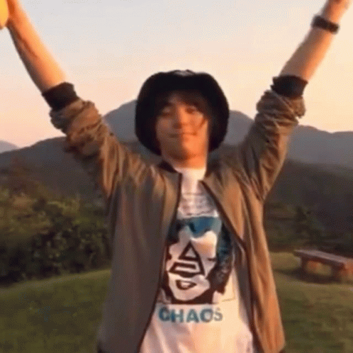 A Man Wearing A Chaos T-Shirt Holds His Arms Up In The Air GIF