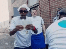 A Man Wearing A Chef 'S Hat And Sunglasses Stands In Front Of A Brick Building GIF