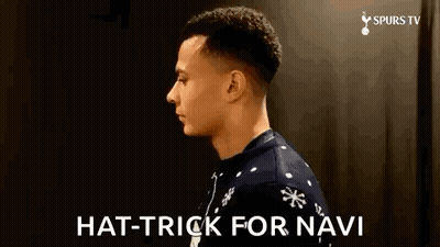 A Man Wearing A Christmas Sweater Is Standing In Front Of A Black Wall And Says `` Hat Trick For Navi '' . GIF