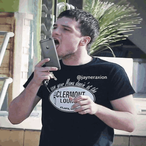 A Man Wearing A Clermont Lounge T-Shirt Is Holding A Cell Phone In His Mouth GIF