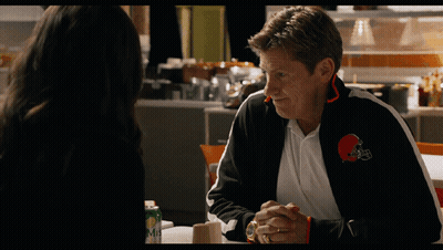 A Man Wearing A Cleveland Browns Jacket Is Talking To A Woman GIF
