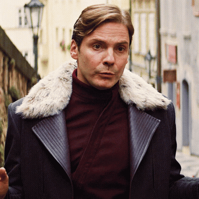 A Man Wearing A Coat With A Fur Collar Is Walking Down A Street GIF