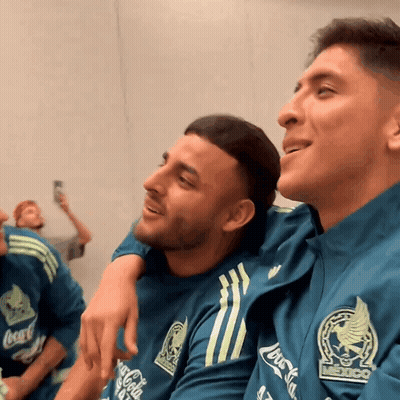 A Man Wearing A Coca Cola Shirt Sits Next To Another Man Wearing A Mexico Shirt GIF