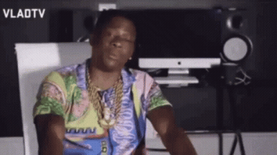 A Man Wearing A Colorful Shirt And A Gold Chain Is Sitting In Front Of A Computer . GIF