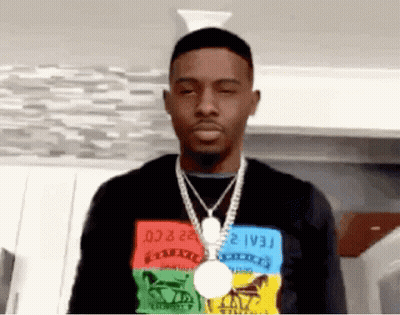 A Man Wearing A Colorful Shirt And A Necklace Is Standing In A Room . GIF