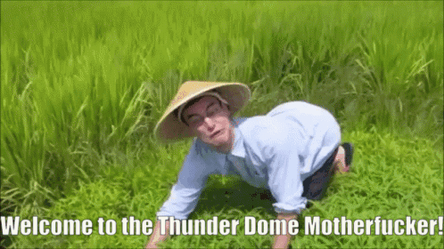 A Man Wearing A Conical Hat Is Kneeling In The Grass With The Words Welcome To The Thunder Dome Motherfucker Written Bel GIF