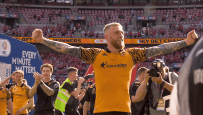 A Man Wearing A Corvindun Jersey Stands In Front Of A Blue Sign That Says Every Minute Matters GIF