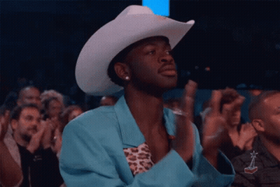 A Man Wearing A Cowboy Hat And A Blue Jacket Is Applauding In A Crowd . GIF