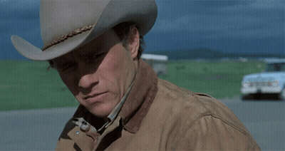 A Man Wearing A Cowboy Hat And A Jacket Looks Down GIF