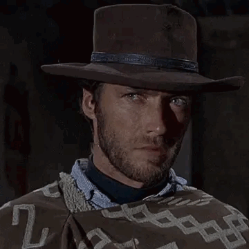 A Man Wearing A Cowboy Hat And A Poncho Is Holding A Chain Around His Mouth . GIF
