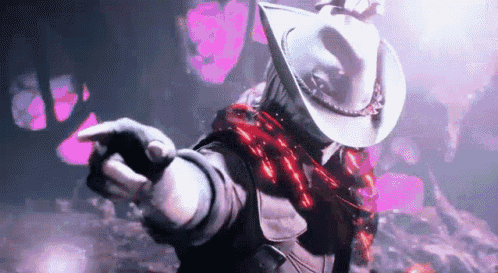 A Man Wearing A Cowboy Hat And A Scarf Is Pointing At Something . GIF