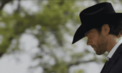 A Man Wearing A Cowboy Hat And A Suit Is Looking Down GIF