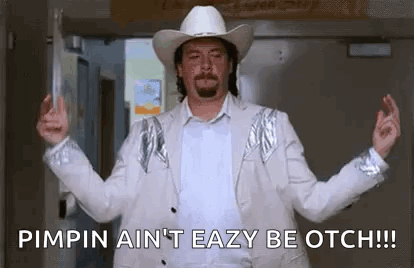 A Man Wearing A Cowboy Hat And A White Suit Is Standing In A Doorway With His Arms Outstretched . GIF