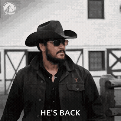 A Man Wearing A Cowboy Hat And Sunglasses Is Standing In Front Of A Building And Saying `` He 'S Back '' . GIF