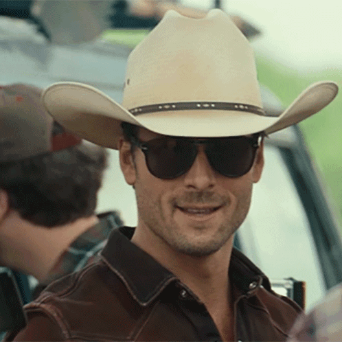 A Man Wearing A Cowboy Hat And Sunglasses Looks At The Camera GIF