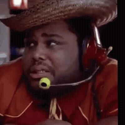 A Man Wearing A Cowboy Hat And Tie With A Green Object In His Mouth Is Looking At The Camera . GIF