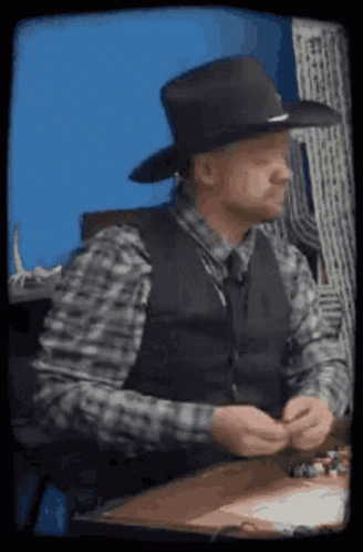 A Man Wearing A Cowboy Hat And Vest Is Sitting At A Table GIF