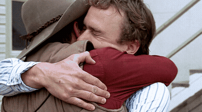 A Man Wearing A Cowboy Hat Is Hugging Another Man GIF